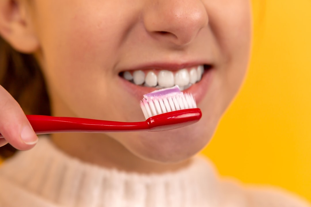 A red toothbrush with purple toothpaste is held near a person's smiling mouth