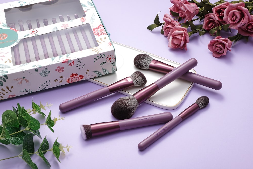 Purple makeup brushes with a box, tray, and roses on a purple surface