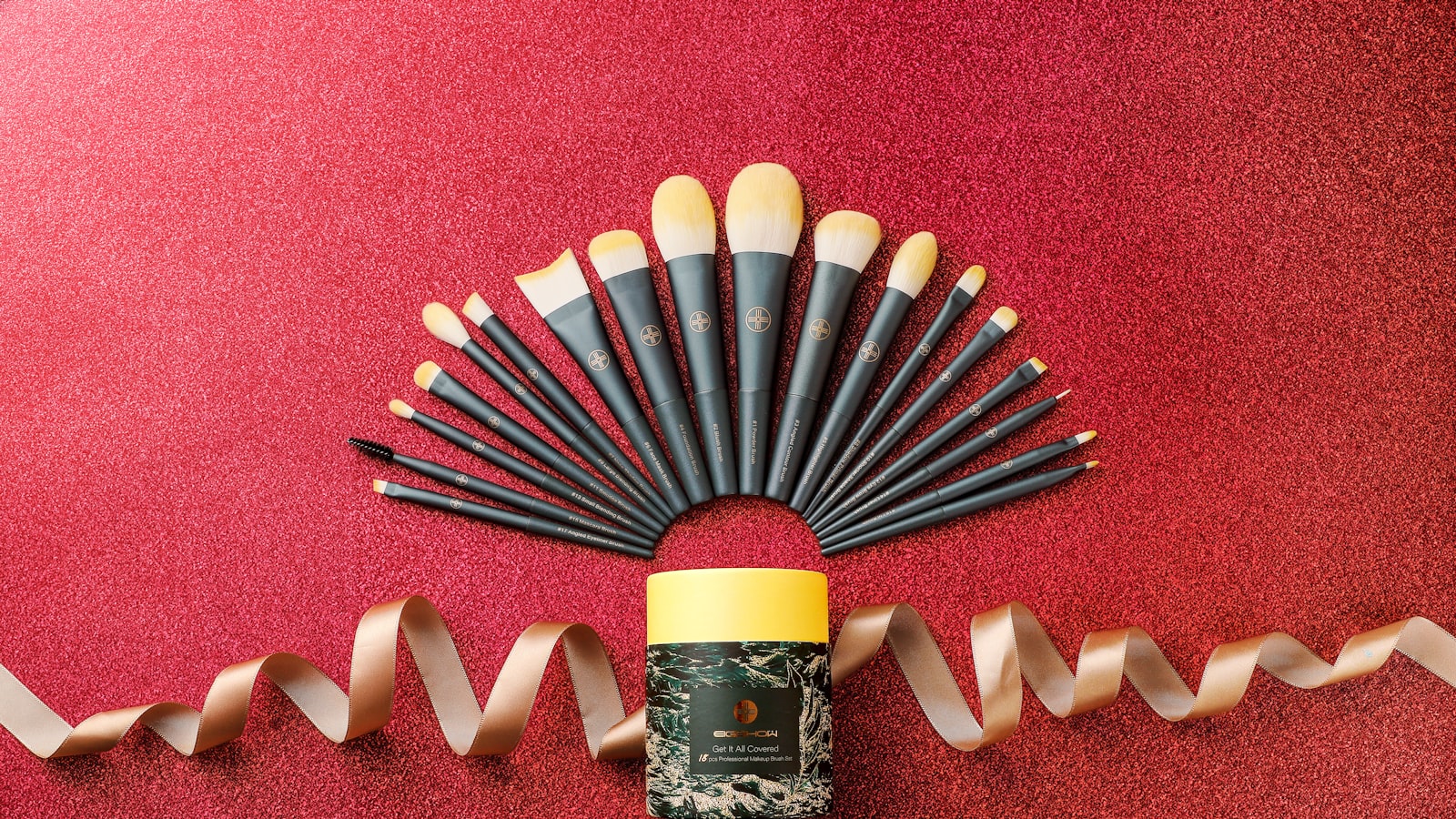 Makeup brushes fan out above a cylindrical container on a red glitter surface