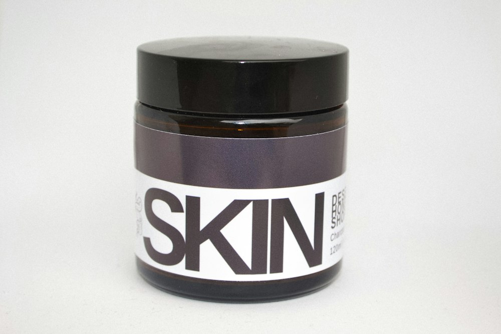 A brown glass jar with a black lid and a white label reading SKIN