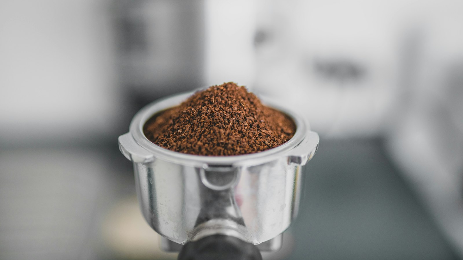An espresso portafilter filled with a mound of ground coffee beans