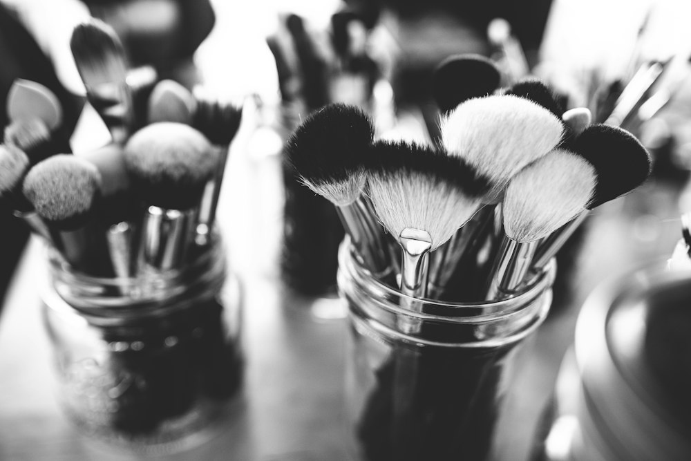 A grayscale, close-up shot of two glass jars filled with various makeup brushes