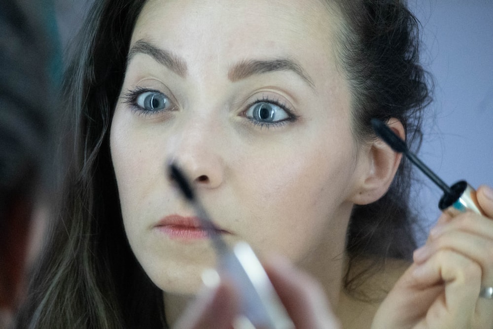 A person holds a mascara brush near their eyes in a close-up shot