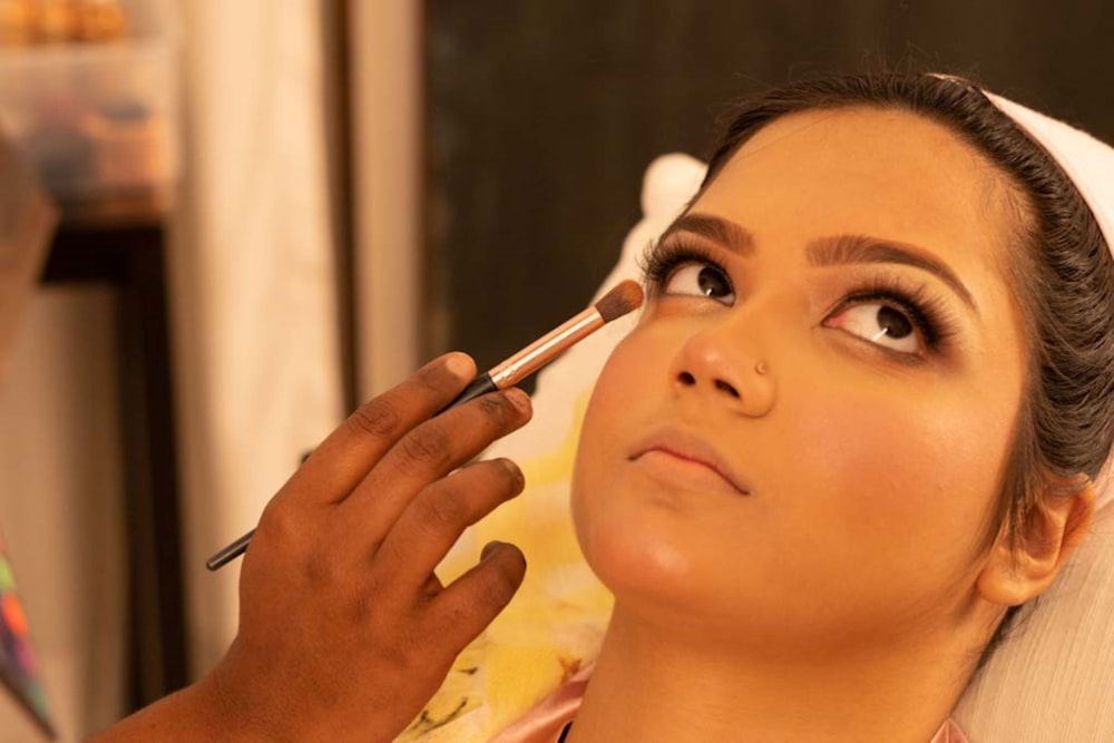 A person applies makeup to another person's eye area with a brush