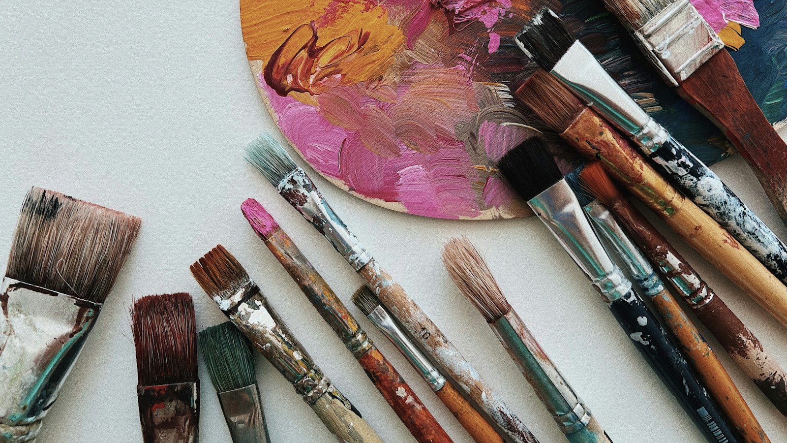 Overhead view of an artist's palette smeared with colorful paint, surrounded by various paintbrushes