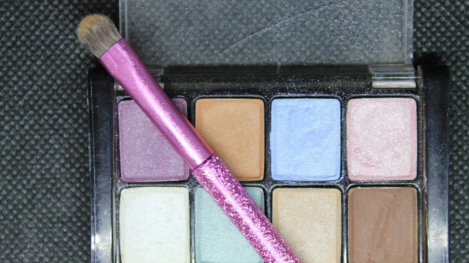 A glittery pink makeup brush rests diagonally across an open eyeshadow palette