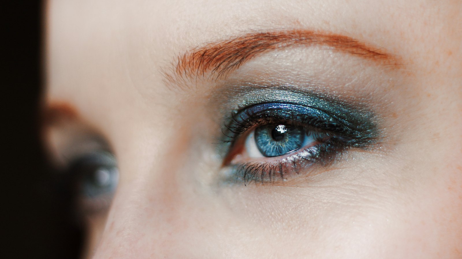 Close-up of a blue eye with metallic green and blue eyeshadow and a red eyebrow