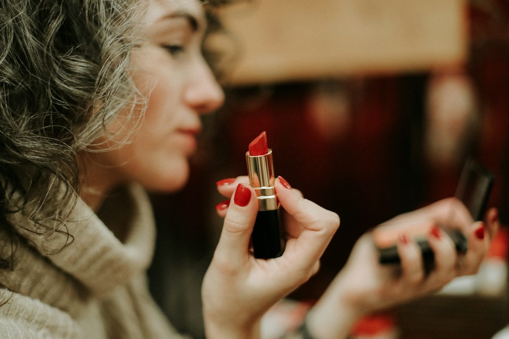 A woman with curly grey hair holding a tube of red lipstick