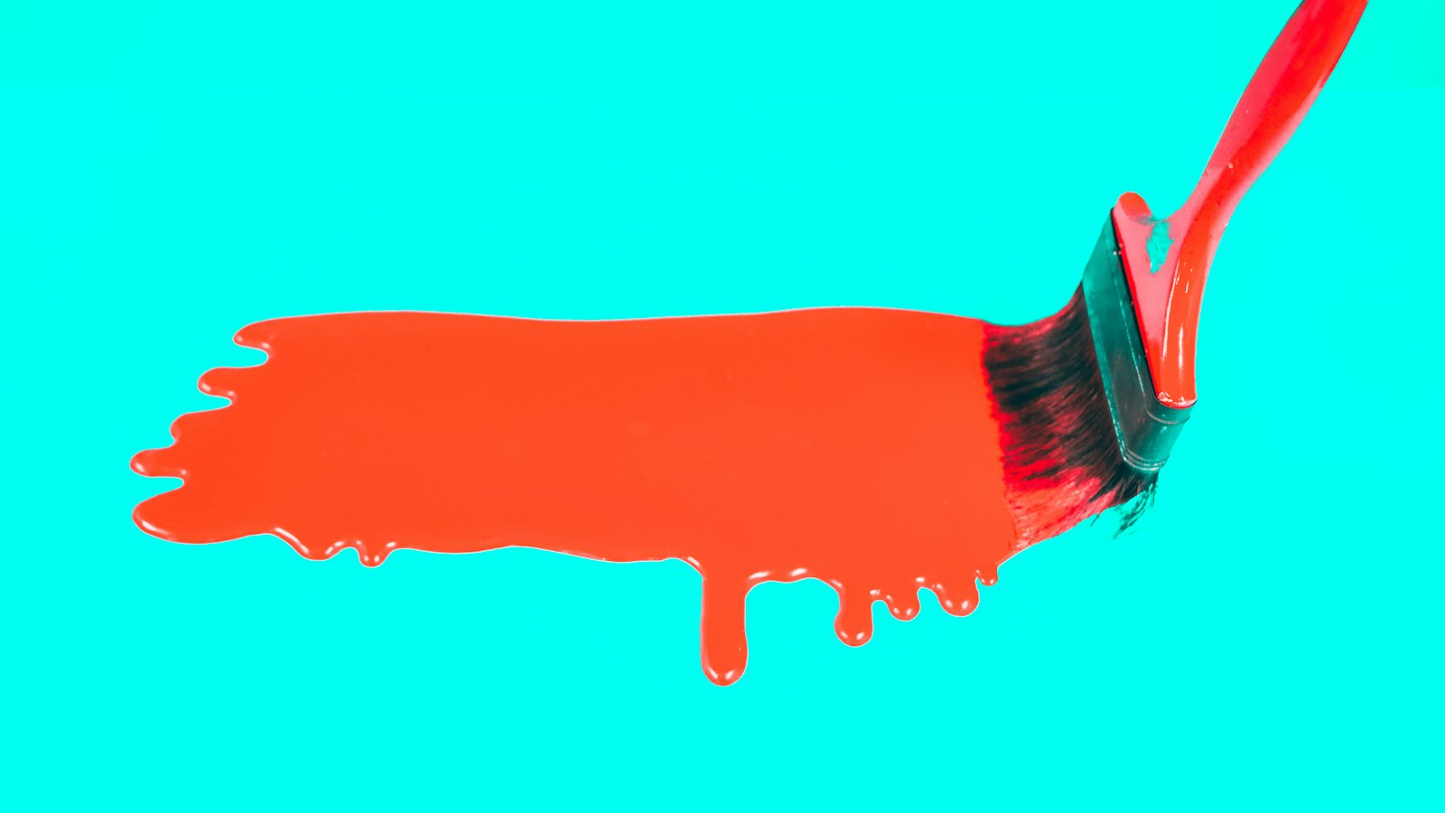 A red paintbrush spreads red paint across a bright blue surface