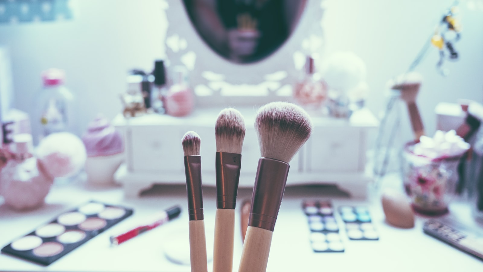 Three makeup brushes stand upright before a vanity with cosmetic products